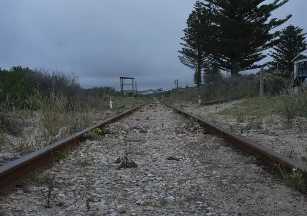 Train tracks shot from a low angle. They look old and decrepit, rusty in colour with weeds growing in the trackbed.
