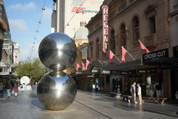 A close up of a sculpture known colloquially as 'the malls balls', two large shiny spheres stacked on on top of the other. They stand approximately 3.5m high. In the background are several shops.
