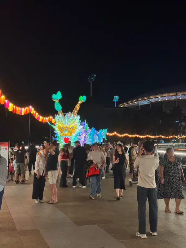 A Chinese dragon installation atop a bridge at night-time. It is lit from within. It has many vibrant colours