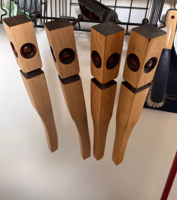 four table legs, hanging on a hook, they have been coated in tung oil making them look slightly darker