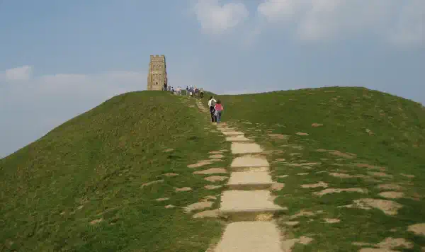 A view up a grassy hill, a small stone tower at the top