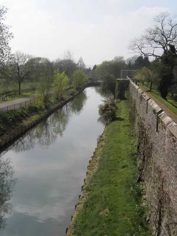 A stone wall on the right goes into the distance. On the left is a moat, running parallel.