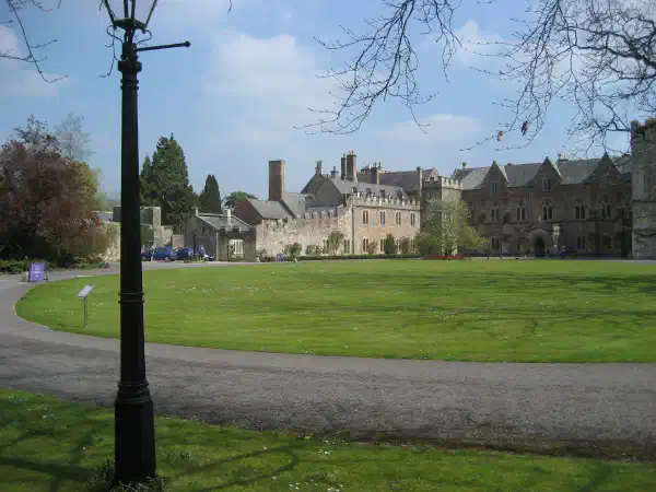 A road sweeps around from the right to the left and off to the distance. In the background is a large manor house