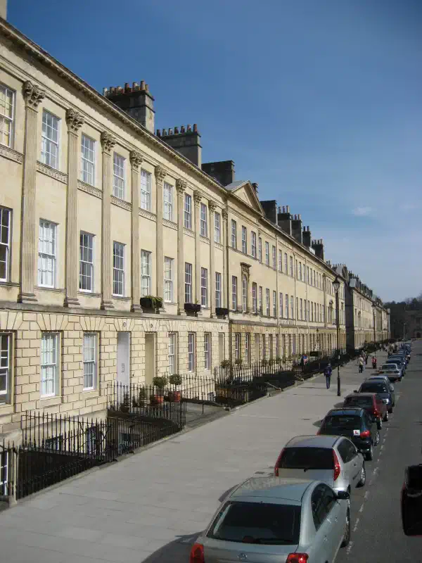 A view of a city street in Bath. On the left are many yellow fronted buildings, all adjoining and uniform.