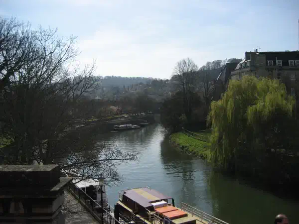 A river curves around to the right in the distance. There are boats on the river and trees on the riverbank. Some buildings are visible through the trees on the far side.