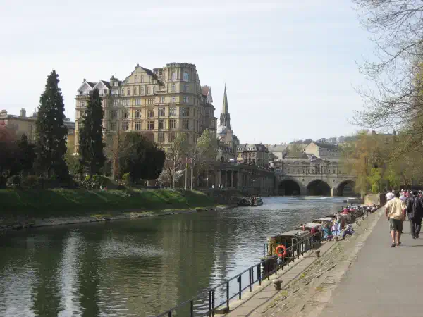 Riverside view, people walk on the path and old buildings are in the background